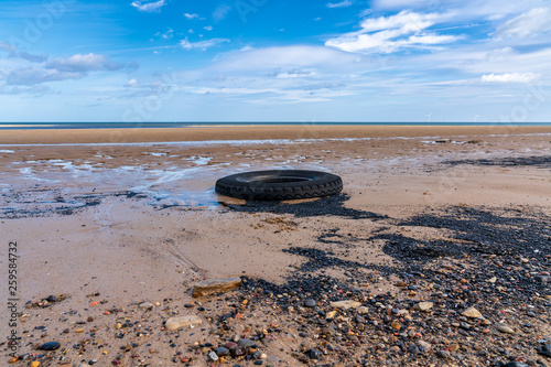 North Sea coast in Cambois, Northumberland, England, UK - and old tyre on the beach with wind turbines in the background