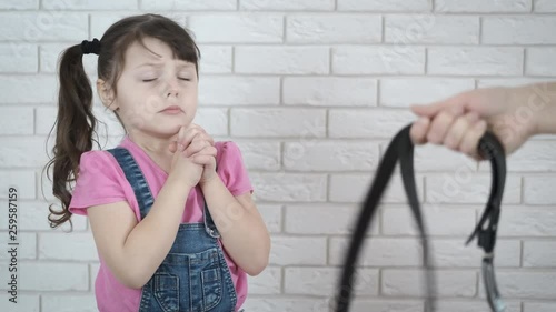 Child abuse. The child is threatened with beating. A pleading little girl on the background of a leather belt in the hands of parents.