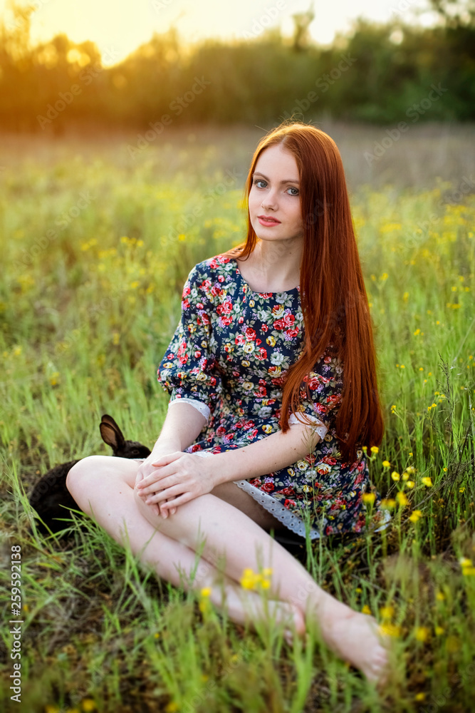 young redhead girl with a black rabbit on a flowering meadow in the rays of the setting sun young redhead girl with a black rabbit on a flowering meadow in the rays of the setting sun