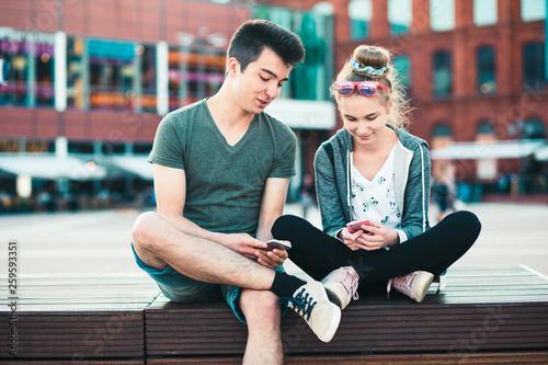 Couple of friends, teenage girl and boy, having fun together with smartphones