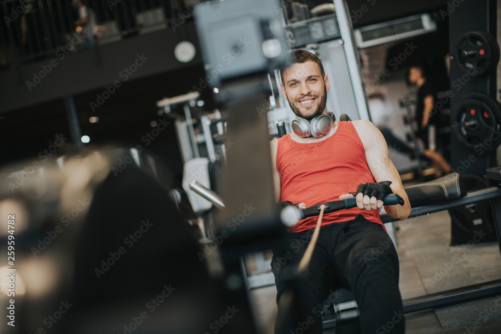 Young man doing workouts on a back with power exercise machine in a gym club