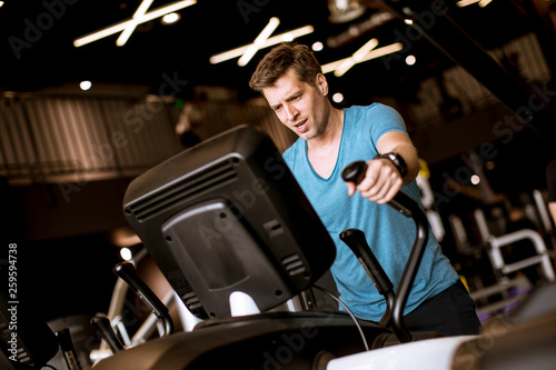 Man doing exercise on elliptical cross trainer in sport fitness gym club