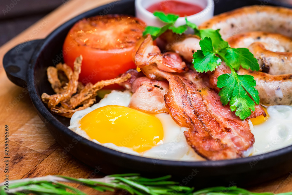 Nutritious meal with fried egg, sausage, bacon, tomato and sauce in frying pan