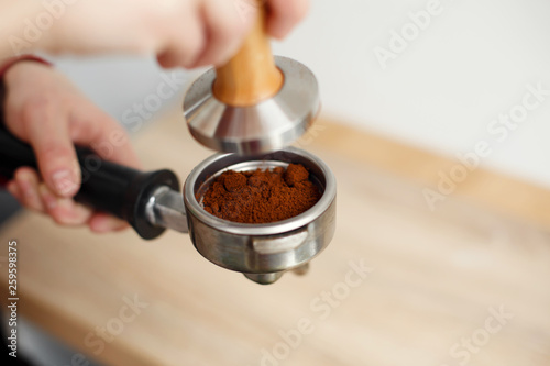 Fototapeta Naklejka Na Ścianę i Meble -  close-up barista hand tamps ground coffee with tamper a into the holder for the coffee machine
