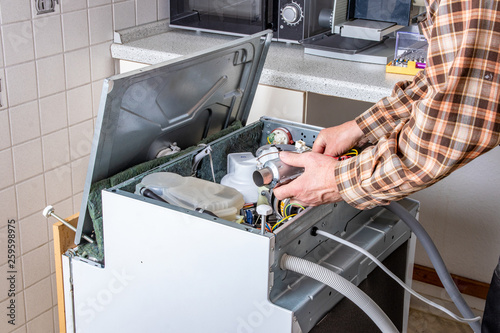 People in technician jobs. Appliance repair technician or handyman works on broken dishwasher in a kittchen. Laborer is changing the heating element. photo