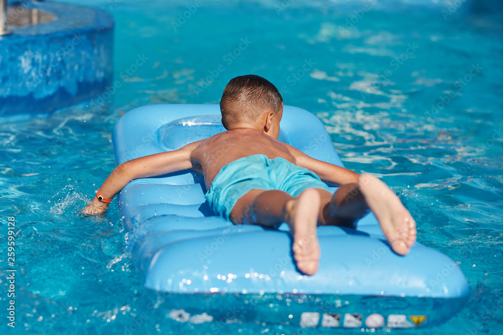 Boy relaxing on inflatable mattress at hotel swimming pool in summer ...