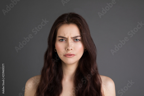 Close up portrait of beautiful girl with brunette hair frowning her face in displeasure with bare shoulders