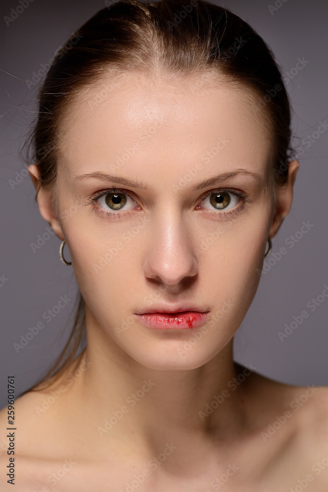 portrait of a young beautiful girl with blood on her lips, on a gray background.