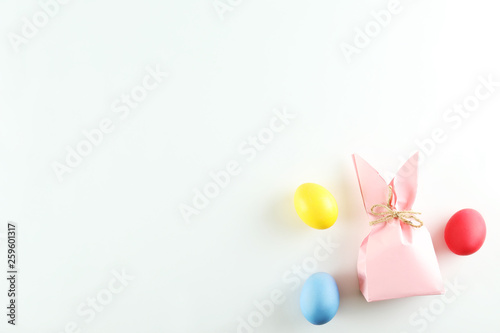 Pink Easter present box in a form of bag with bunny ears in minimal top view composition with colored chicken eggs, bright paper background. A lot of copy space for text. Close up, flat lay.