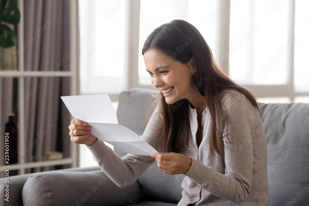 Fototapeta premium Excited woman sitting on couch reading letter great news