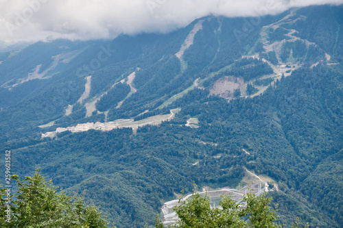 Sports facilities and residential buildings on the slope of a high mountain with a green slope and the top in the clouds. A sports and tourist base in the mountains.