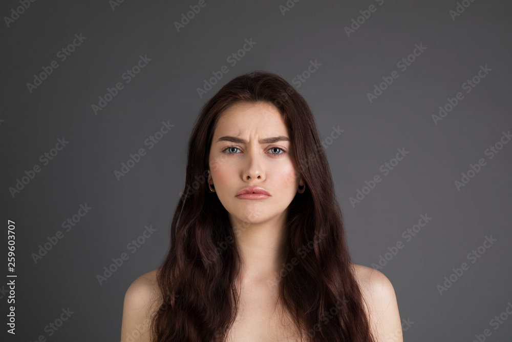 Close up portrait of offended unhappy beautiful woman with long brunette hair, bare shoulders