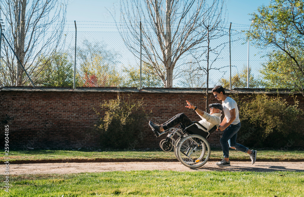 56 year old male sitting on a wheelchair and he young friend happy in the park 56 year old male sitting on a wheelchair and he young friend happy in the park