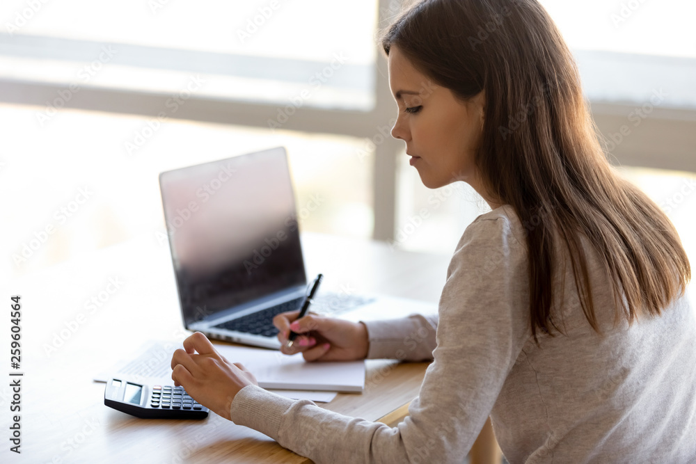 Side rear view young female sitting at table calculating money