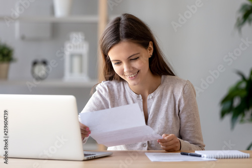 Happy satisfied woman sitting at desk reading positive letter