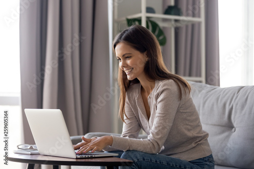 Smiling female sitting on couch having fun in internet