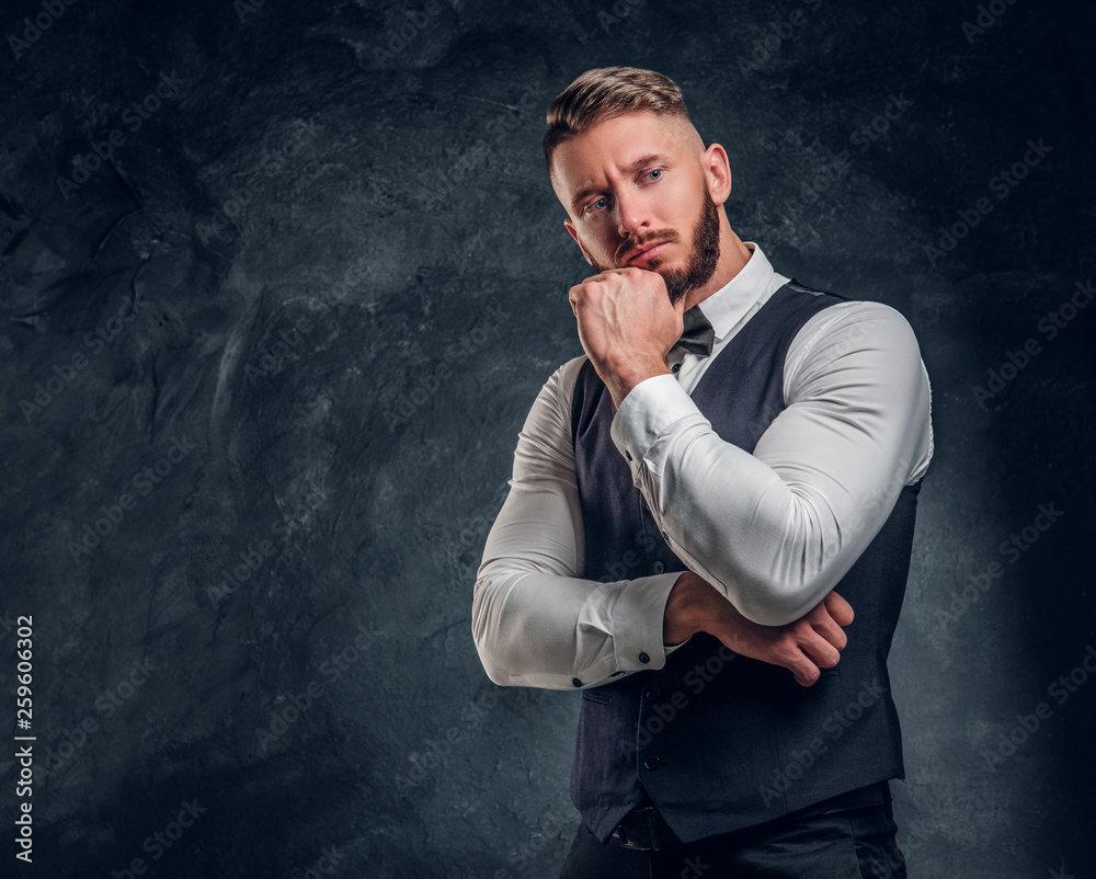 Pensive male thinking about something important. Elegantly dressed young man in a vest with bow tie posing with hand on chin. Studio photo against a dark wall background Pensive male thinking about something important. Elegantly dressed young man in a vest with bow tie posing with hand on chin. Studio photo against a dark wall background