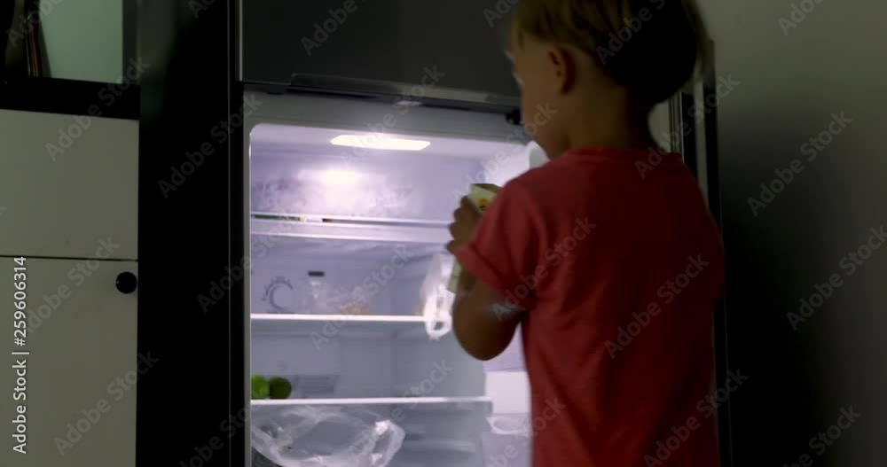 Little boy stands open refrigerator selects product. Boy picks up box milk leaves Little boy stands open refrigerator selects product. Boy picks up box milk leaves