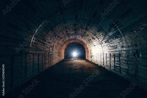 Dark creepy abandoned underground tunnel or vault corridor in bomb shelter and man with flashlight, abstract light in end concept