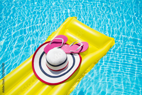 Beach summer holiday background. Inflatable air mattress, flip flops and hat on swimming pool. Yellow lilo and summertime accessories on poolside. Top view and copy space © ladyalex