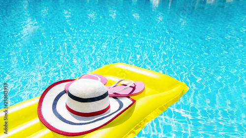 Beach summer holiday background. Inflatable air mattress, flip flops and hat on swimming pool. Yellow lilo and summertime accessories on poolside. Top view and copy space. Selective focus. Banner