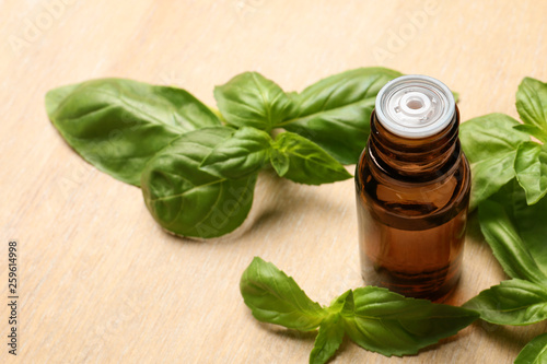 Bottle of basil essential oil and fresh leaves on wooden table. Space for text