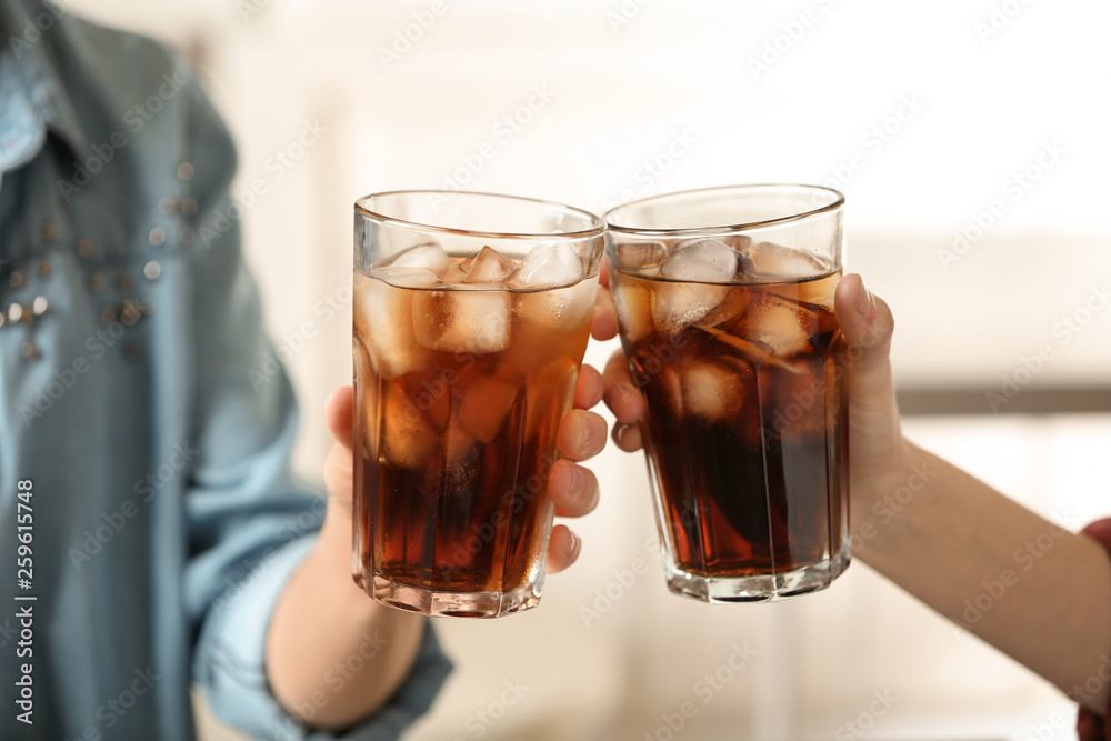 Women holding glasses of cola with ice on blurred background, closeup Women holding glasses of cola with ice on blurred background, closeup