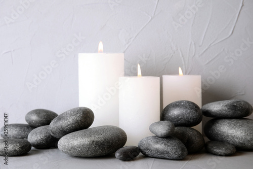 Zen stones and lighted candles on table against light background