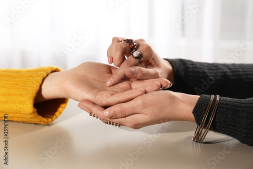 Chiromancer reading lines on woman's palm at table, closeup photo