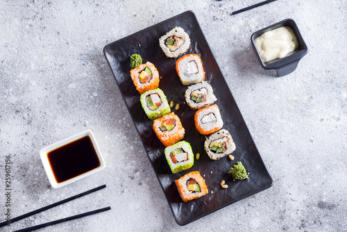 Various Fresh and delicious sushi set on black slate with metal and slate sticks, sauce on light stone background , flat lay copy space