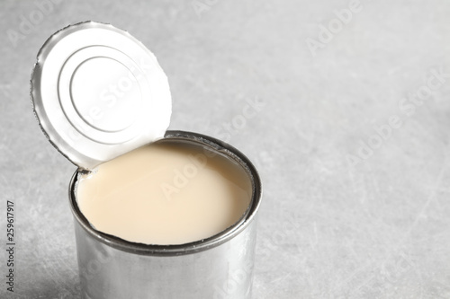 Tin can with condensed milk on grey background, space for text. Dairy product