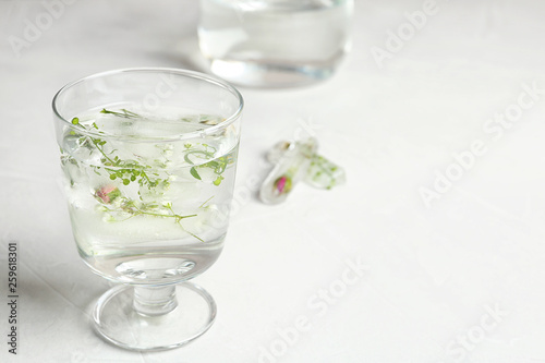 Glass of water and floral ice cubes on table. Space for text
