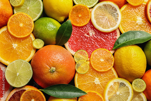 Fototapeta Naklejka Na Ścianę i Meble -  Sliced and whole citrus fruits with leaves as background, top view