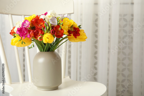 Vase with bouquet of spring freesia flowers on chair in room. Space for text