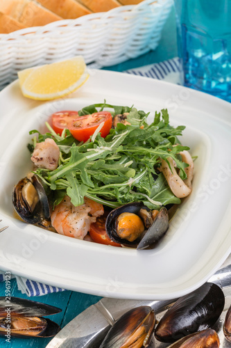Seafood salad, mussels, shrimp and arugula on a blue wooden background