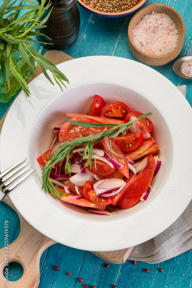 Delicious summer salad with fresh tomatoes and red onions, decorated with a sprig of tarragon, on a blue wooden background Delicious summer salad with fresh tomatoes and red onions, decorated with a sprig of tarragon, on a blue wooden background