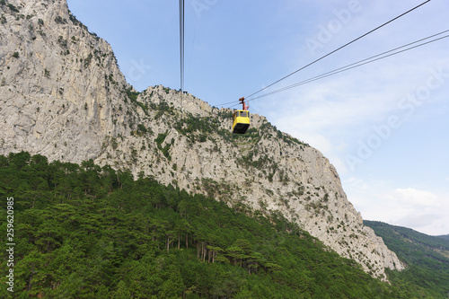 Yellow cableway tourist cable car rises to the top of the high Crimean mountain AI-Petri. The rocks were overgrown with pine trees