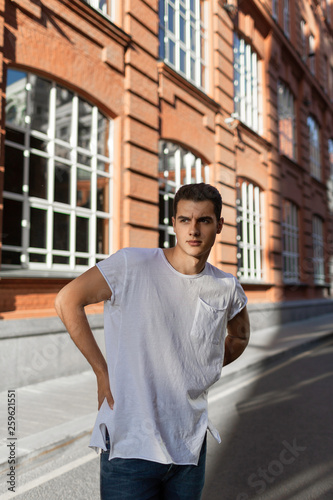 Beautiful caucasian man in white t-shirt and blue jeans stay on the street 
