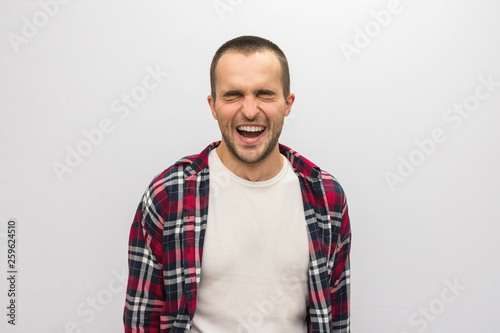 Attractive guy in plaid shirt smiling, closing his eyes with joy, open his mouth, front view, white background with copy space, for advertising