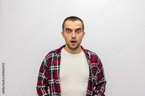 Attractive guy in plaid shirt having opened a mouth from shock, looking at camera, front view, white background with copy space, for advertising