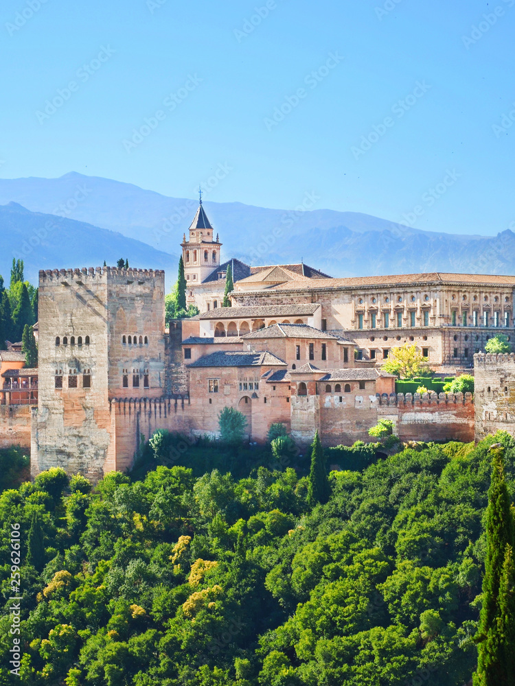 Vertical picture of beautiful Alhambra Palace complex in Granada, Spain. The amazing sample of Moorish architecture is surrounded by woods and mountains. Taken with blue sky above.