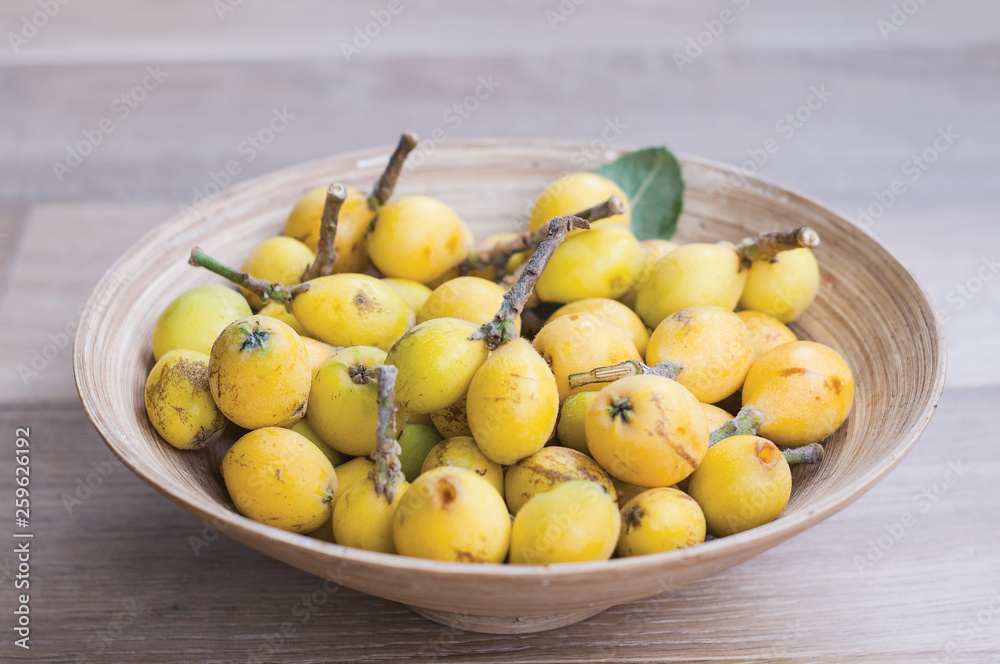 The vertical photo of Japanese fruit, loquat, in a bowl on the wooden background The vertical photo of Japanese fruit, loquat, in a bowl on the wooden background