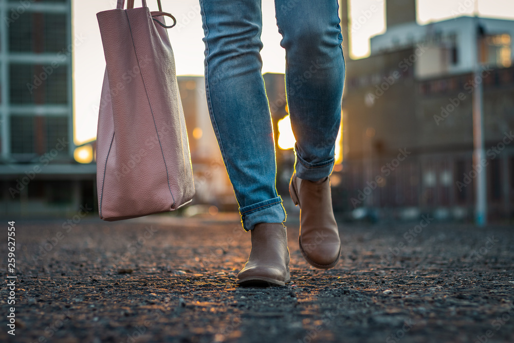 Woman in jeans and stylish leather shoe with bag walking in city during sunset Woman in jeans and stylish leather shoe with bag walking in city during sunset