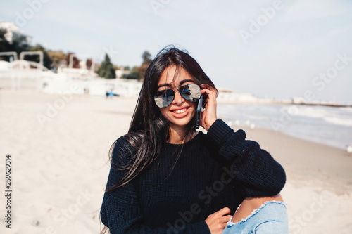 Young woman talking on mobile phone on a beach with ocean sea background.nice smile beautiful middle age lonely woman enjoy the beach sitting on a seat with ocean in background. using smartphone  © ClaudiK
