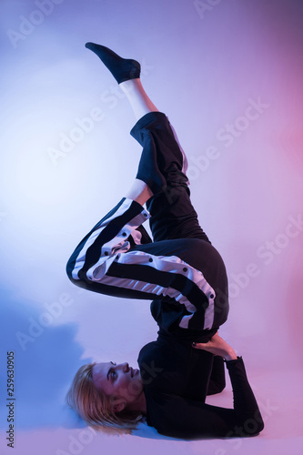 Young girl with legs in air and sports tracksuits shows his gymnastic skills on colorful background and studio red and blue lights. Low key setup