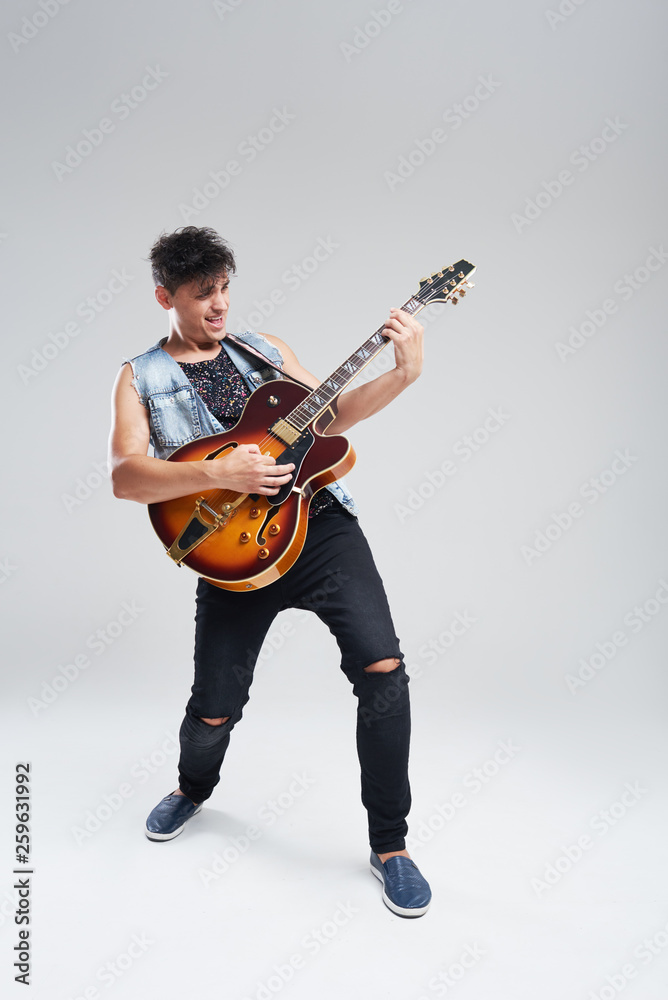 Young man musician with an electric guitar in hand on a gray background. he plays rock and roll loudly. Full-length portrait. Young man musician with an electric guitar in hand on a gray background. he plays rock and roll loudly. Full-length portrait.