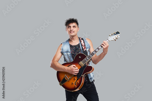 Young man musician with an electric guitar in hand on a gray background. he plays rock and roll loudly. 