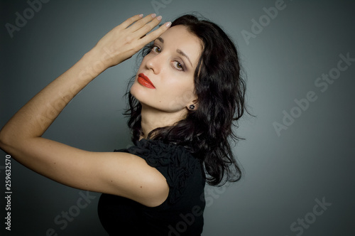 Amazing young girl with red sensual lips and dark hair posing on black background in studio