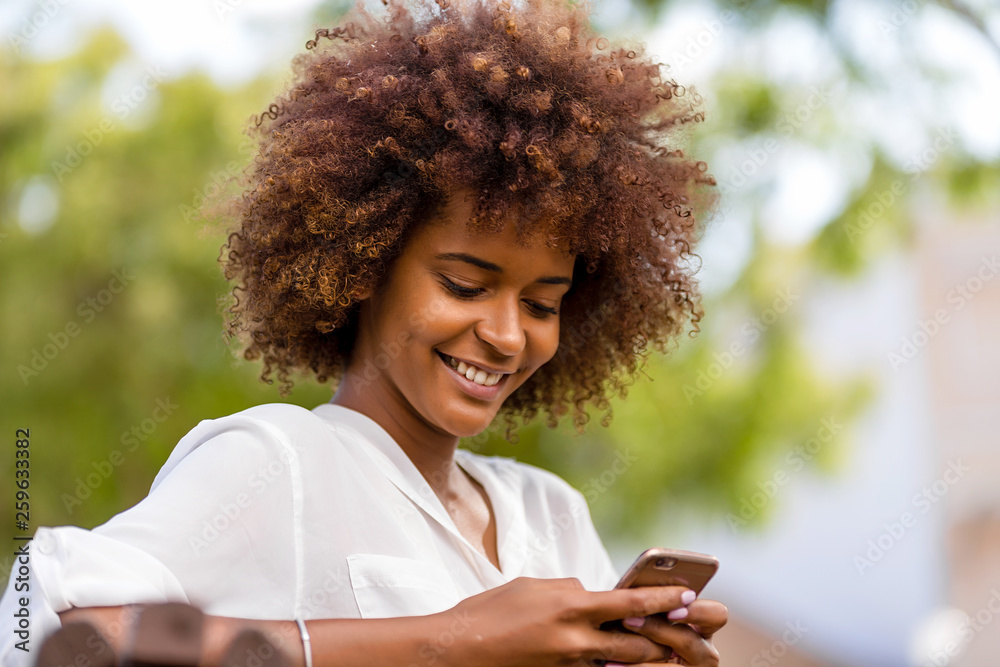 Outdoor portrait of a Young black African American young woman texting ...