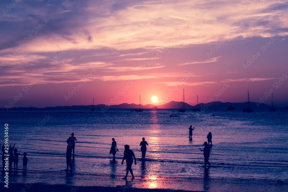 Pink toned. Sun path on the water of sea. Tropical island and sandy beach with silhouette of a lot of tourists. Enjoy of sunrise
